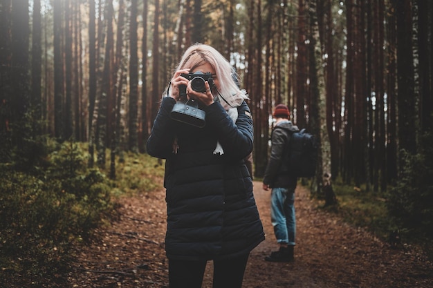 Młoda blond kobieta robi zdjęcie aparatem podczas spaceru po lesie z przyjaciółmi.