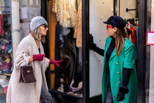 Młoda blondynka korzystających z zakupów w mieście i obecności sprzedawcy, patrząc przez okno sklepów odzieżowych. Okulary przeciwsłoneczne i czerwone rękawiczki
