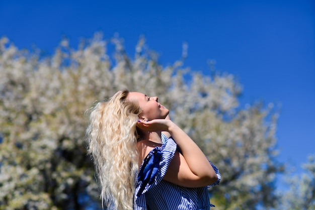 Młoda blondynka patrzy na piękne błękitne niebo i sięga do niego rękami. Piękna suczka podziwia naturę.