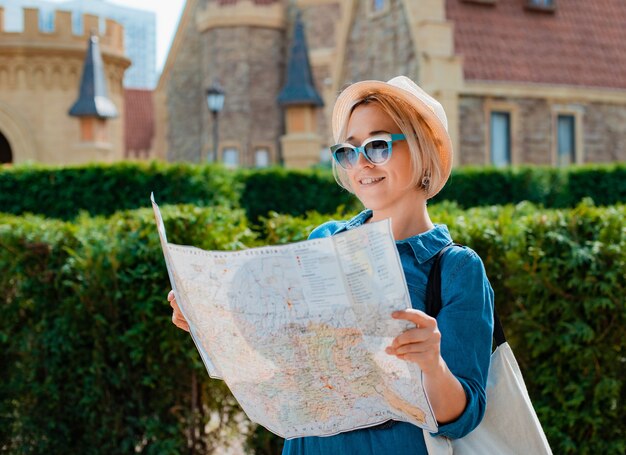 Zdjęcie młoda blondynka podróżnik kobieta w kapeluszu i okularach przeciwsłonecznych z mapą zabytków innego kraju. letnie wakacje i aktywny wypoczynek wolność i koncepcja aktywnego stylu życia