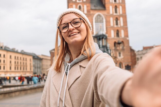 Młoda blondynka robi sobie selfie na telefonie komórkowym na placu rynkowym w Krakowie w Polsce.