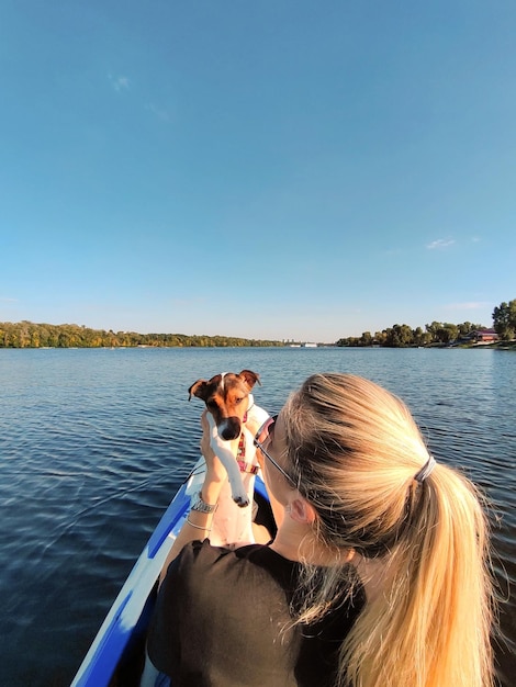 Młoda blondynka trzyma na ramieniu psa Jack Russell terriera Pływają łodzią po szerokiej rzece Turystyka i rekreacja z zwierzętami domowymi