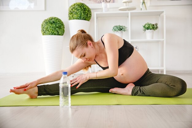 Młoda blondynka w ciąży uprawia sport w domu na macie. Wysokiej jakości zdjęcie