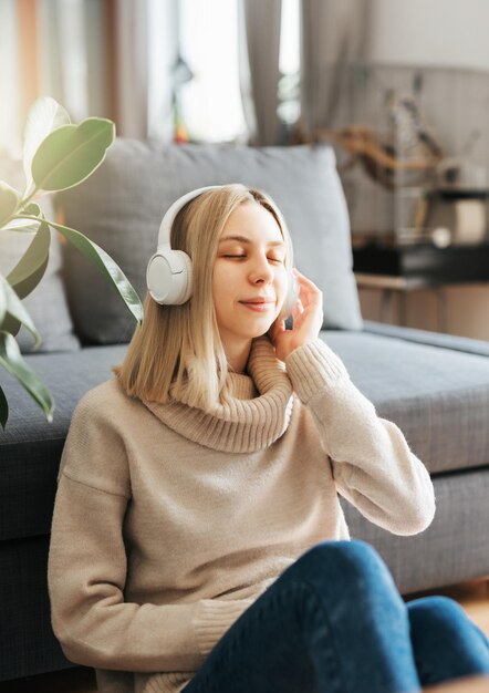 Młoda blondynka w słuchawkach słucha muzyki i relaksuje się w domu.
