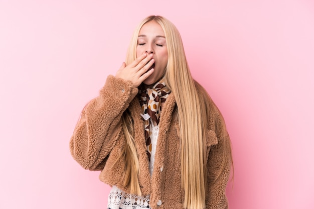 Młoda blondynki kobieta jest ubranym żakiet przeciw różowemu ściennemu ziewaniu pokazuje zmęczonego gest zakrywającego usta ręką.