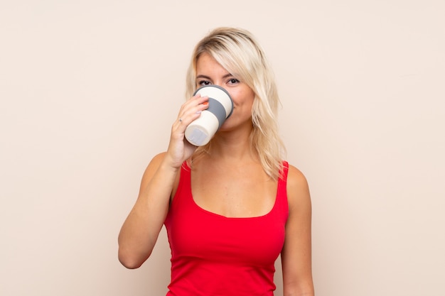 Młoda blondynki kobieta nad odosobnioną ścianą trzyma kawę i pije zabrać