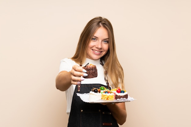 Młoda blondynki kobieta nad odosobnioną ścianą trzyma mini torty i oferuje je
