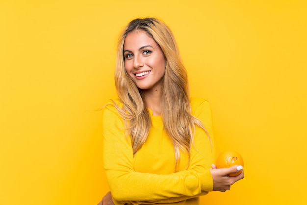 Młoda blondynki kobieta trzyma pomarańcze nad kolor żółty ścianą
