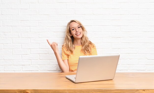 Młoda blondynki kobieta uśmiecha się szczęśliwie i patrzeje z ukosa, zastanawia się, myśleć lub ma pomysł używać laptopu