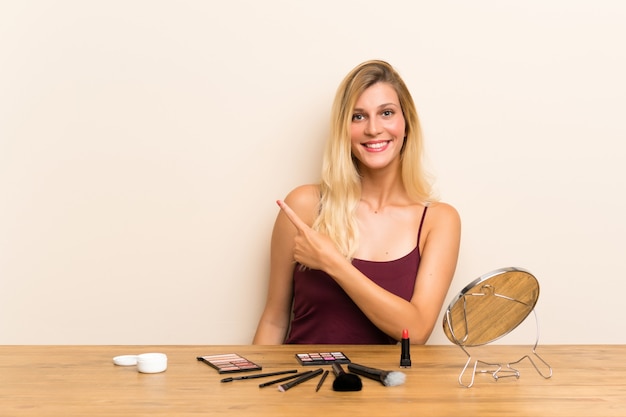 Młoda blondynki kobieta z kosmetykiem w stołowym wskazuje palcu strona