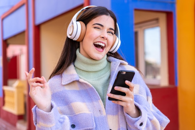 Młoda Brazylijka na zewnątrz słucha muzyki za pomocą telefonu komórkowego i śpiewa