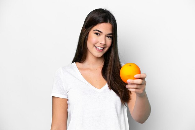 Młoda brazylijska kobieta trzyma pomarańczę na białym tle ze szczęśliwym wyrazem twarzy