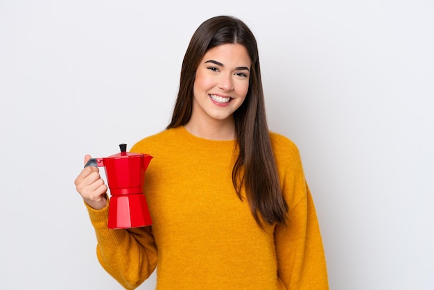 Młoda brazylijska kobieta trzymająca dzbanek do kawy na białym tle uśmiecha się dużo