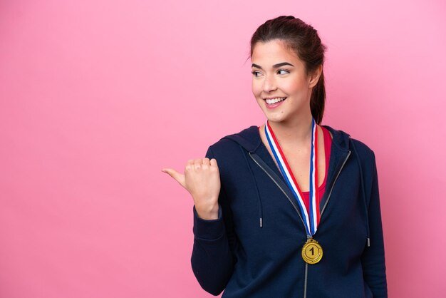 Młoda brazylijska sportowa kobieta z medalami na białym tle na różowym tle skierowana w bok, aby zaprezentować produkt