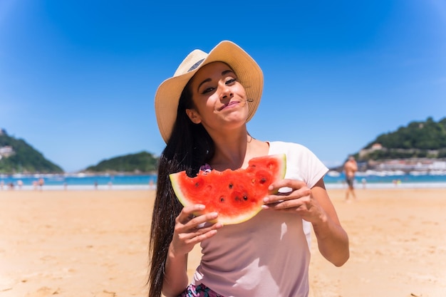 Młoda brunetka Kaukaska kobieta je arbuza na plaży na letnie wakacje