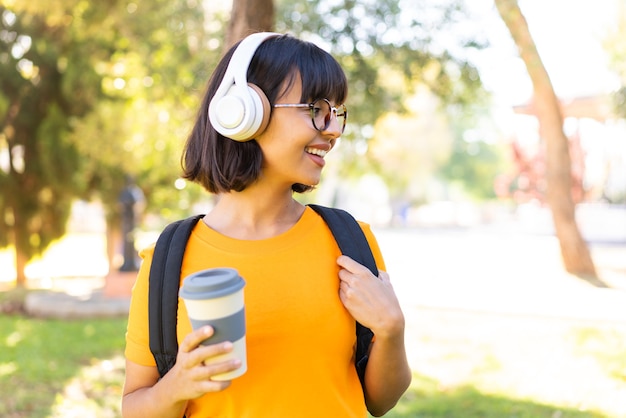 Młoda brunetka kobieta na zewnątrz słucha muzyki i trzyma kawę na wynos