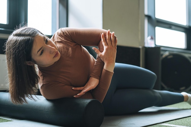 Zdjęcie młoda brunetka kobieta robi rozciąganie pilates na rolce do masażu w siłowni klubu fitness