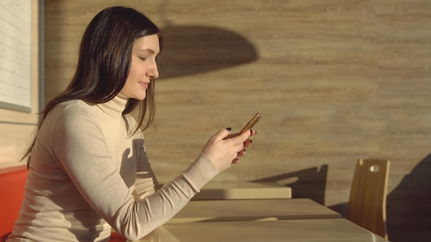 Młoda brunetka kobieta siedzi w kawiarni z telefonem. wirtualna komunikacja.