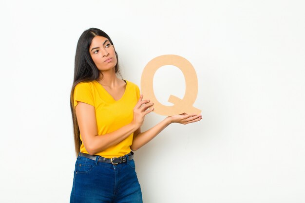 młoda brunetka kobieta trzyma literę Q alfabetu, aby utworzyć słowo lub zdanie