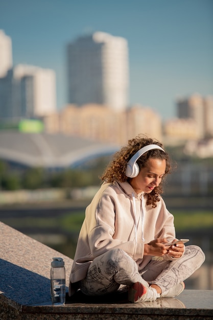 Młoda brunetka kobieta w słuchawkach i odzieży sportowej przewijanie muzyki online podczas wybierania czegoś do posłuchania podczas treningu