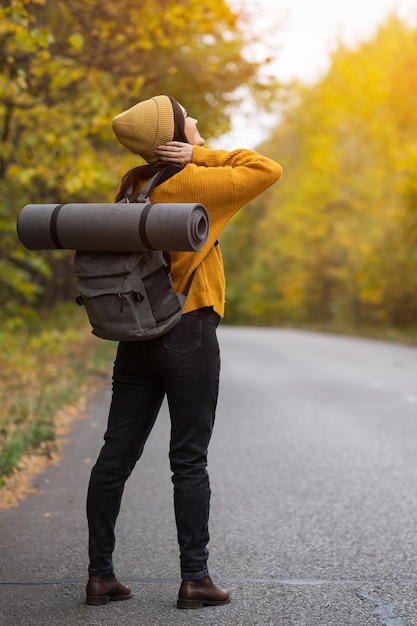 Młoda brunetka kobieta z plecakiem stoi na jesiennej drodze