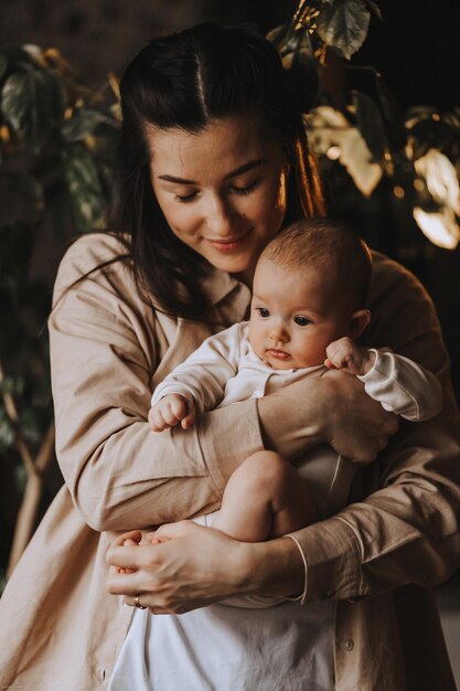 Młoda brunetka mama i jej nowo narodzone dziecko w jej ramionach Zdjęcie domu w ciemnym pokoju przy oknie