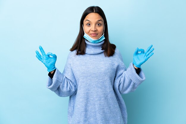 Młoda brunetka mieszanej rasy kobieta ochrony z maską i rękawice na niebieską ścianą w pozie zen
