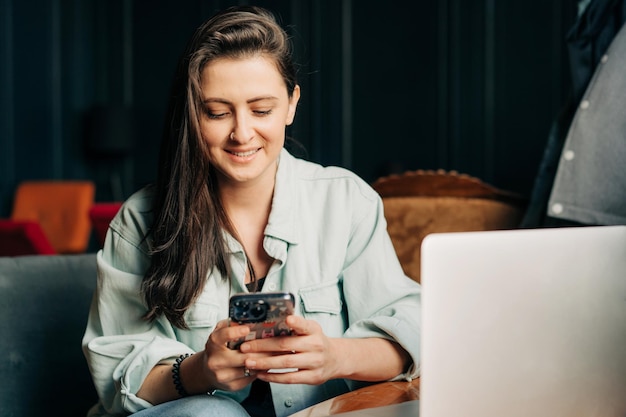 Młoda brunetka siedzi w kawiarni i surfuje w Internecie za pomocą telefonu komórkowego