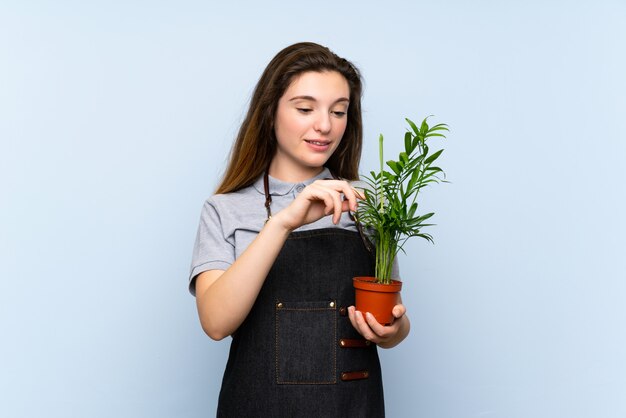 Młoda brunetki dziewczyna nad odosobnioną błękit ścianą bierze flowerpot