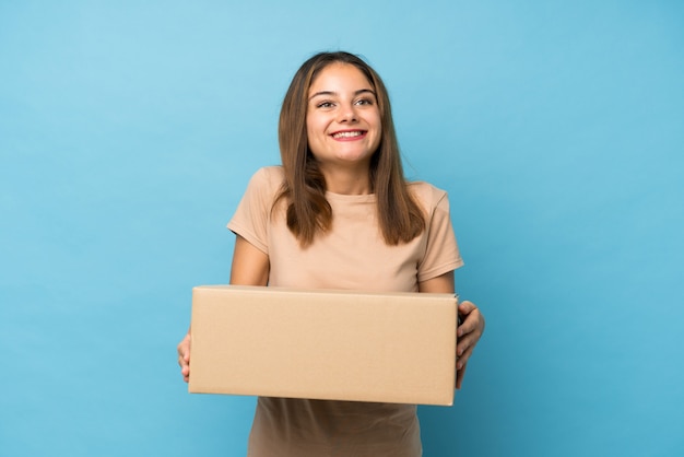 Młoda brunetki dziewczyna nad odosobnionym błękitem trzyma pudełko przenosić je do innego miejsca