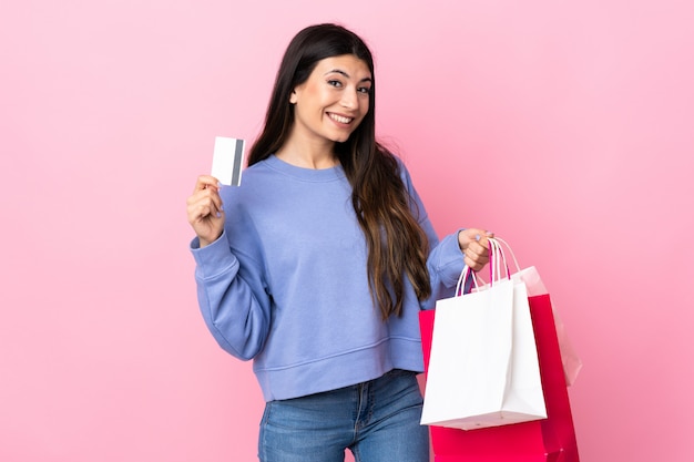 Młoda brunetki dziewczyna nad odosobnionymi menchii ściany mienia torba na zakupy i kartą kredytową