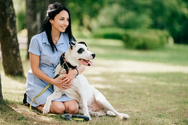 Młoda brunetki dziewczyna ściska jej białego uroczego psa outdoors