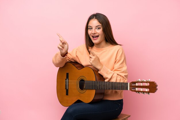 Młoda brunetki dziewczyna z gitarą nad odosobnionymi menchiami zaskakującymi i wskazuje stronę