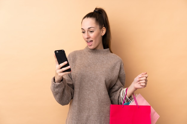 Młoda brunetki kobieta nad odosobnionymi ściennymi mień torba na zakupy i pisać wiadomości z jej telefonem komórkowym przyjaciel