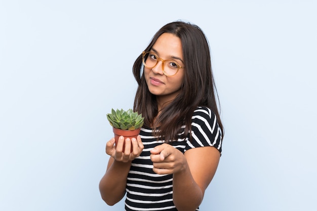 Młoda brunetki kobieta trzyma rośliny wskazuje z ufnym wyrażeniem
