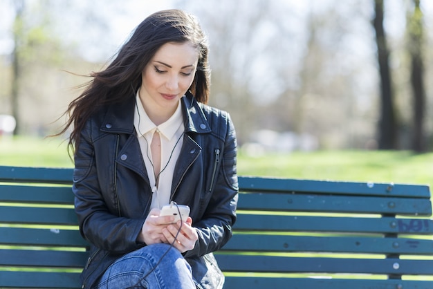 Młoda brunetki kobieta używa jej telefon komórkowego outdoors w parku