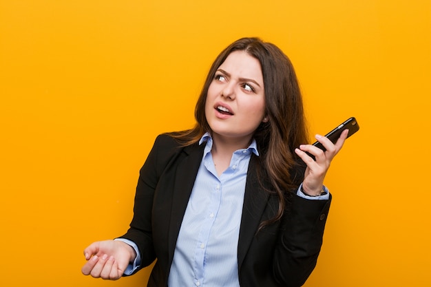 Młoda bujna plus size biznesowa kobieta trzyma telefon próbuje słuchać plotki.