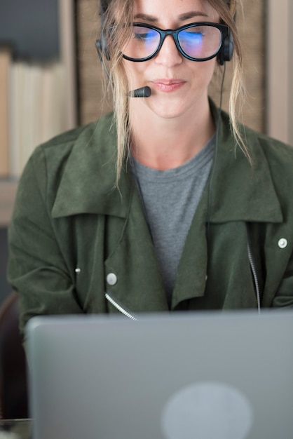 Młoda businesswoman noszenie okularów i zestawu słuchawkowego podczas korzystania z laptopa w miejscu pracy, Piękna kobieta za pomocą laptopa. kobieta nosząca słuchawki z mikrofonem, patrząca na ekran laptopa