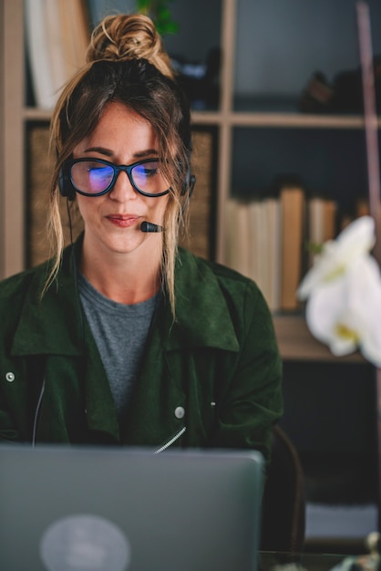 Młoda businesswoman noszenie okularów i zestawu słuchawkowego podczas korzystania z laptopa w miejscu pracy, Piękna kobieta za pomocą laptopa. kobieta nosząca słuchawki z mikrofonem, patrząca na ekran laptopa