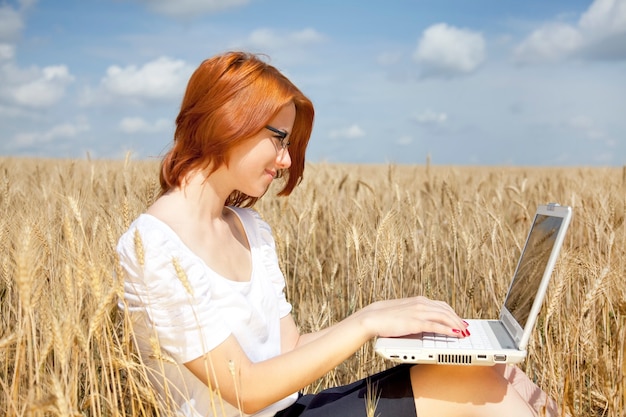 Młoda businesswoman w kolorze białym pracy z notebookiem w polu pszenicy.