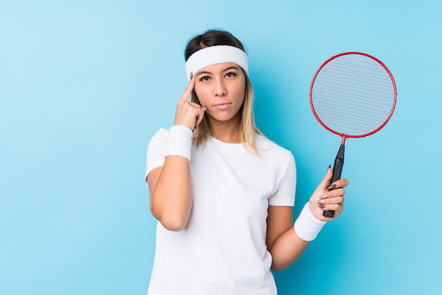 Młoda Caucasian Kobieta Bawić Się Badminton Odizolowywającą Wskazuje świątynię Z Palcem, Główkowanie, Skupiający Się Na Zadaniu.