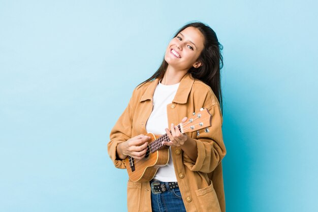 Młoda caucasian kobieta bawić się ukelele odizolowywającego na błękitnej ścianie