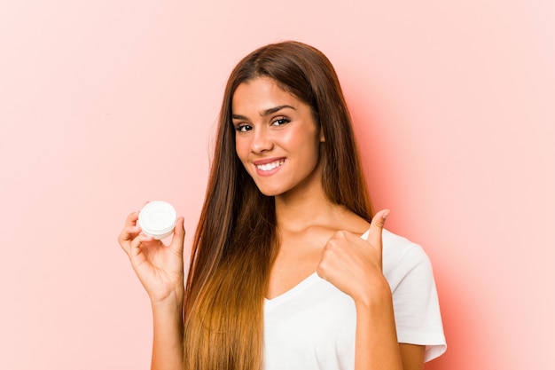 Młoda caucasian kobieta trzyma moisturizer uśmiecha się kciuk up i podnosi
