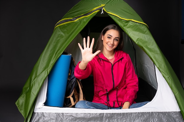 Młoda caucasian kobieta wśrodku campingowego zielonego namiotu liczy pięć z palcami