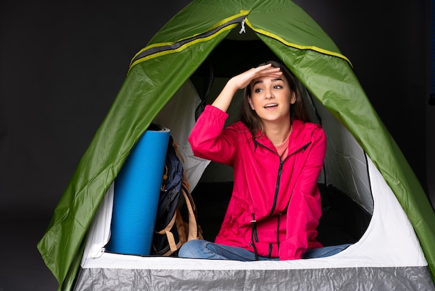 Młoda caucasian kobieta wśrodku campingowego zielonego namiotu patrzeje daleko od ręką patrzeć coś