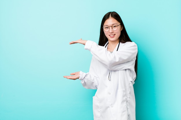 Młoda chińczyka lekarki kobieta szokująca i zadziwiająca trzymająca odbitkową przestrzeń między rękami.