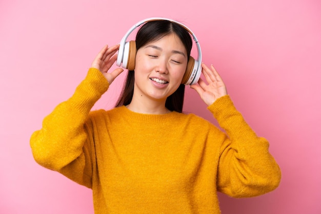 Młoda Chinka odizolowana na różowym tle słuchając muzyki i śpiewając