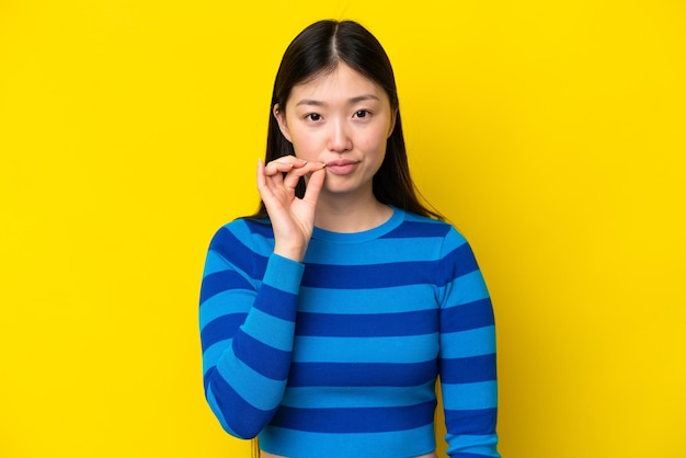 Młoda Chinka odizolowana na żółtym tle, pokazująca znak gestu ciszy