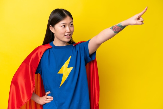 Młoda Chinka odizolowana na żółtym tle w kostiumie superbohatera z dumnym gestem