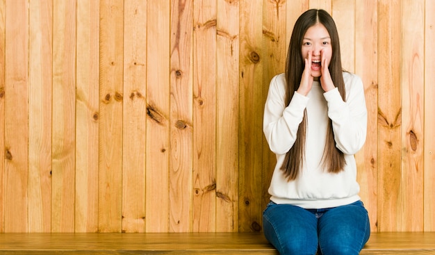 Młoda Chinka siedzi na drewnianym miejscu krzyczy podekscytowany do przodu.